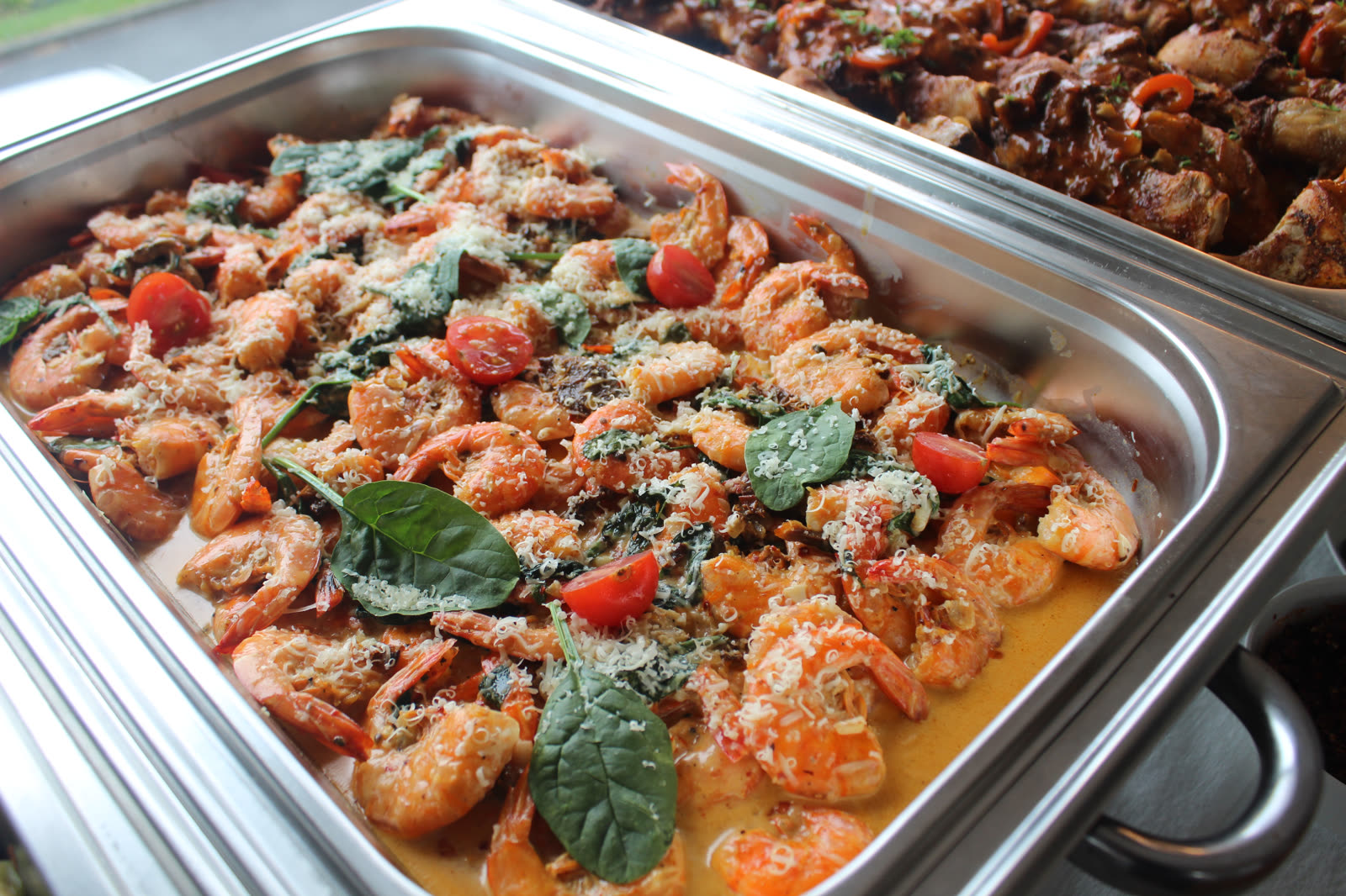 Chafing dish of creamy garlic prawns with spinach and cherry tomatoes